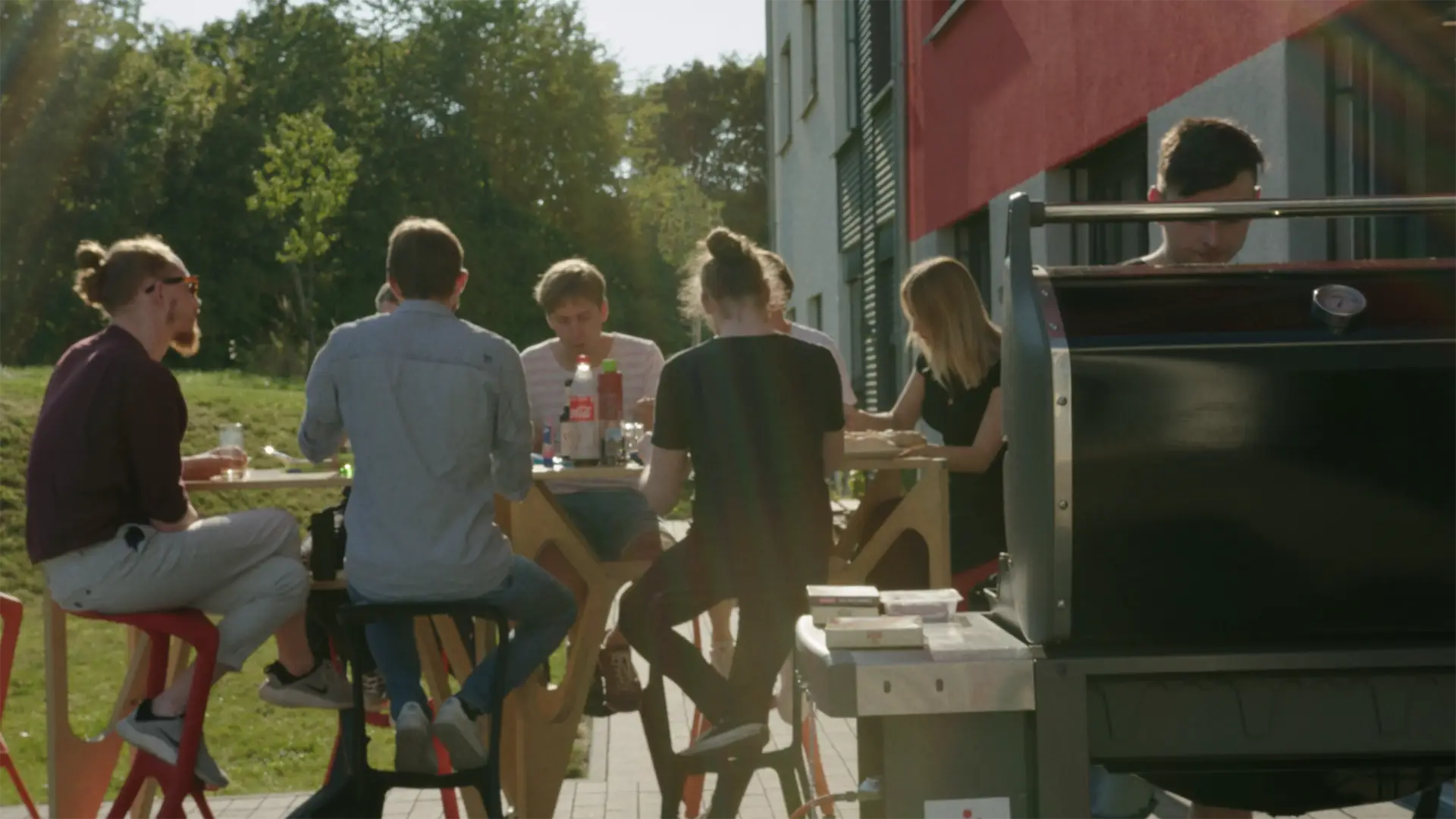 Das Vaira-Team sitzt draußen um einen Tisch versammelt und isst. Im Vordergrund wird ein großer BBQ-Grill bedient.