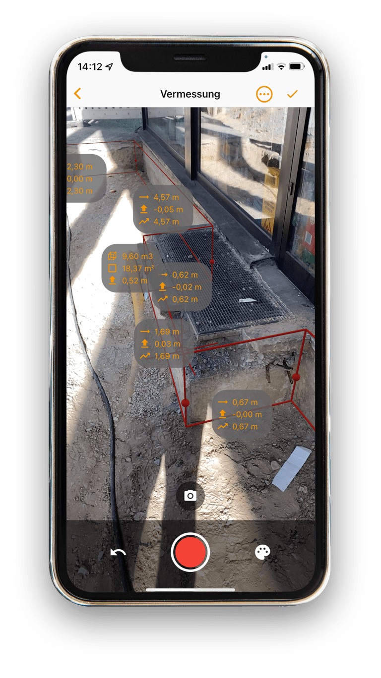 Vaira auf einem iPhone. Zu sehen ist die Vermessung eines L&uuml;ftungsschachts an der Au&szlig;enseite eines Geb&auml;udes, der rundherum freigelegt wurde. Man sieht Vermessungslinien der AR-Vermessung, Fl&auml;chen und auch Kubaturen-Vermessungen und mehrere Distanzmessungen als Zahlen im Bild.