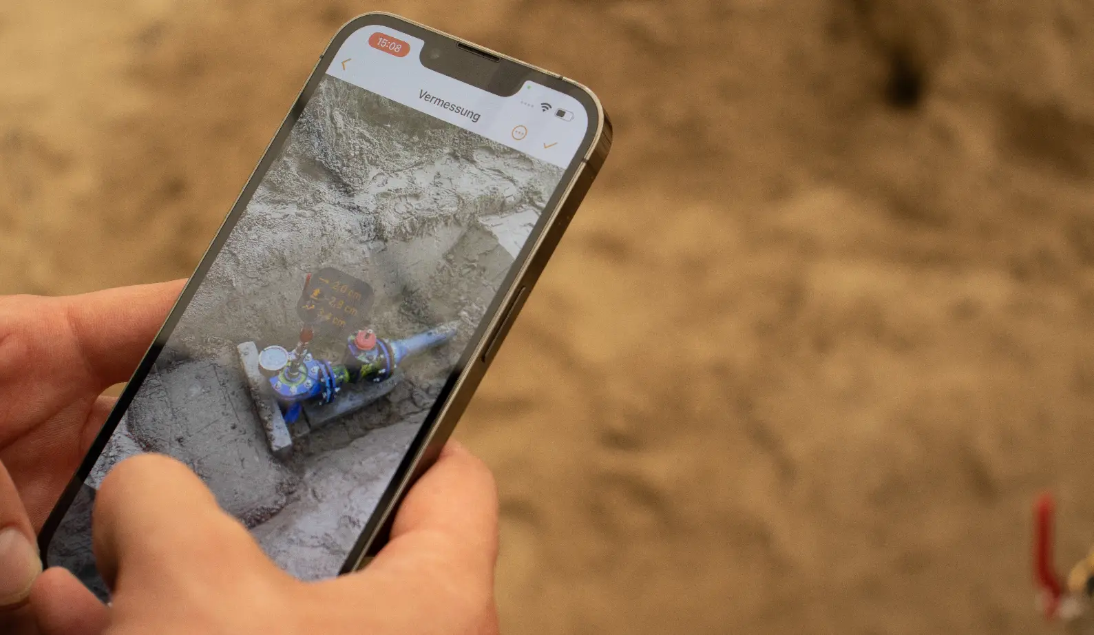 Handwerker mit Smartphone in der Hand vor dem Baugraben