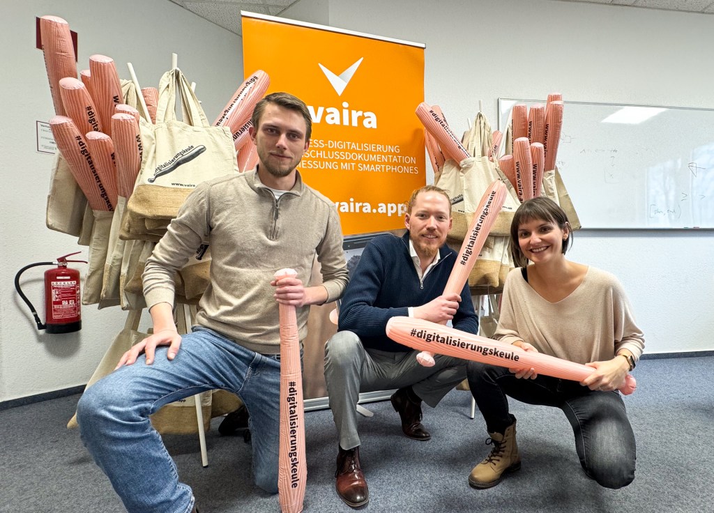 Philipp, Max und Saskia vor einem Vaira-Banner mit ganz vielen eingetüteten Digitalisierungskeulen.