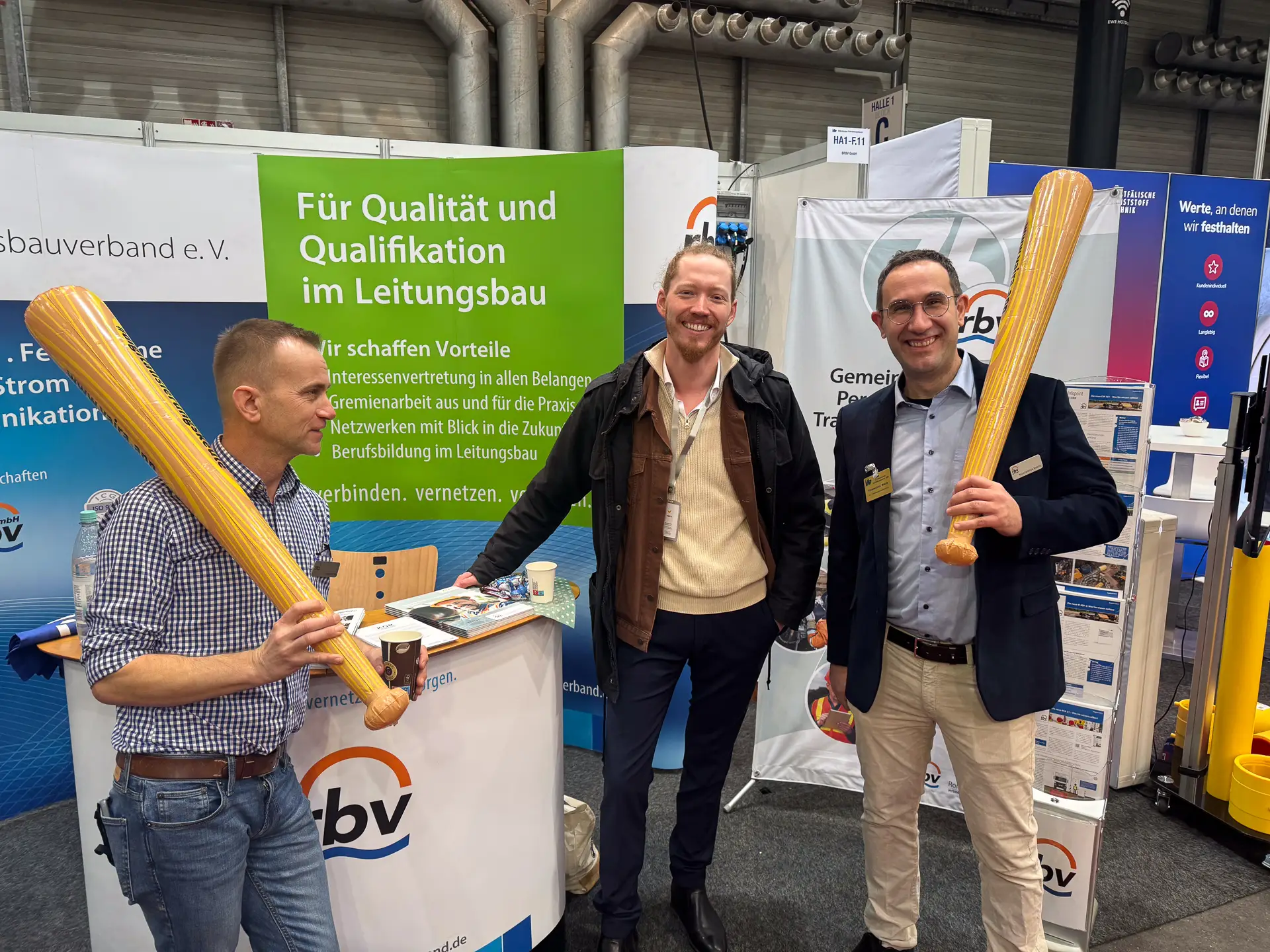 Gruppenfoto – (v.l.) Helge Fuchs (RBV), Max Erdmann (Vaira) und Konstantinos Makris (RBV) am RBV-Stand auf der IRO 2025. Helge und Konstantinos halten eine Digitalisierungskeule von Vaira in der Hand.