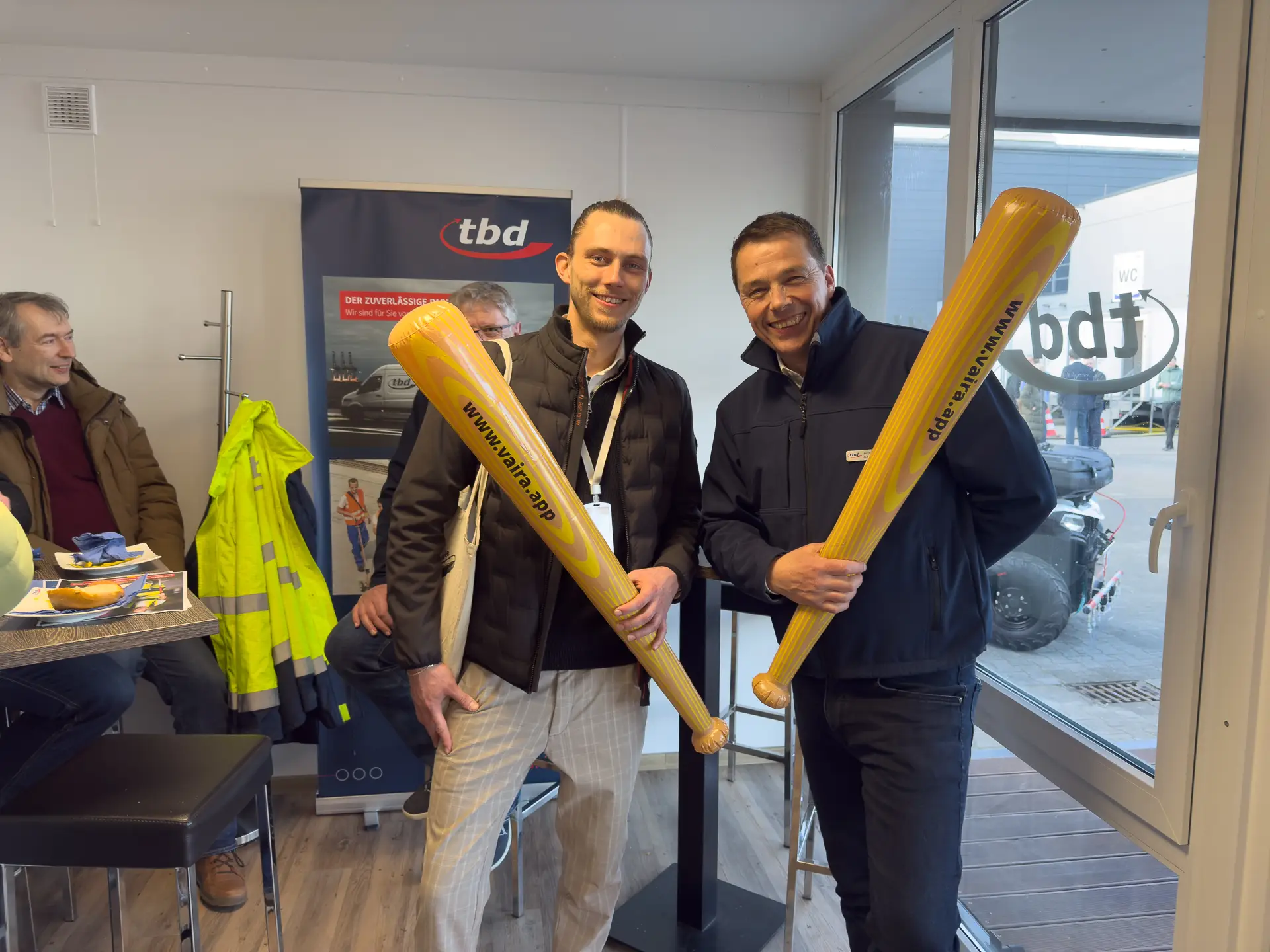 Gruppenfoto – (v.l.) Philipp Buttmann (Vaira) und Arnd Kleemann (tbd) am tbd-Messestand auf der IRO 2025. Beide halten eine Digitalisierungskeule in der Hand.