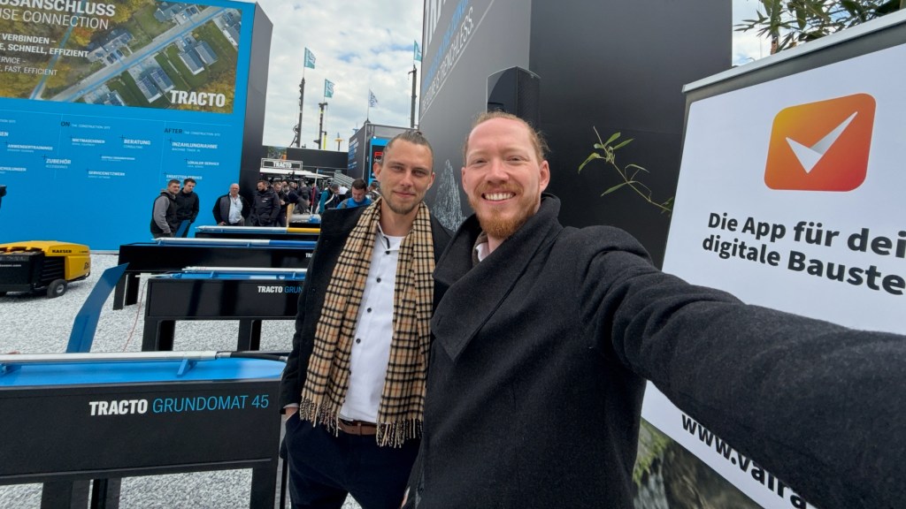 (v.l.) Philipp und Max nebeneinander machen ein Selfie am Partner-Stand von TRACTO neben einem Vaira-Banner auf der bauma 2025 in München.