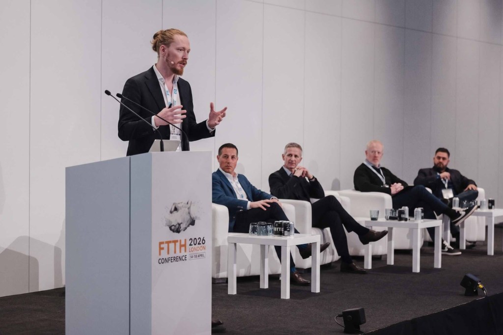 Max referiert auf der FTTH Conference 2026 in London über die digitale Baudokumentation – im Hintergrund sitzen weitere Redner, darunter auch Dario Conforti von Trimble